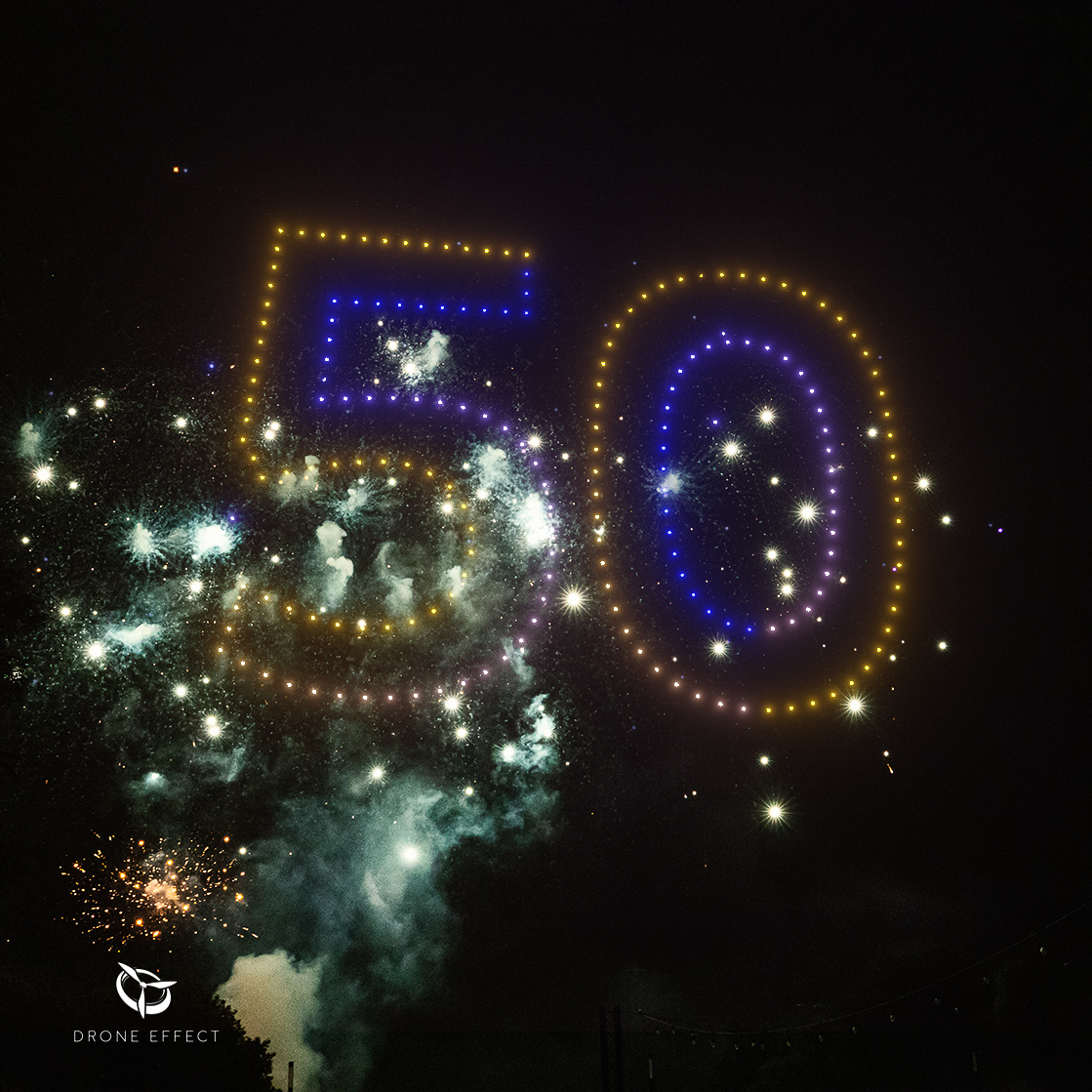 Spectacle hybride combinant 400 drones formant le logo 50 et un feu d’artifice en arrière-plan